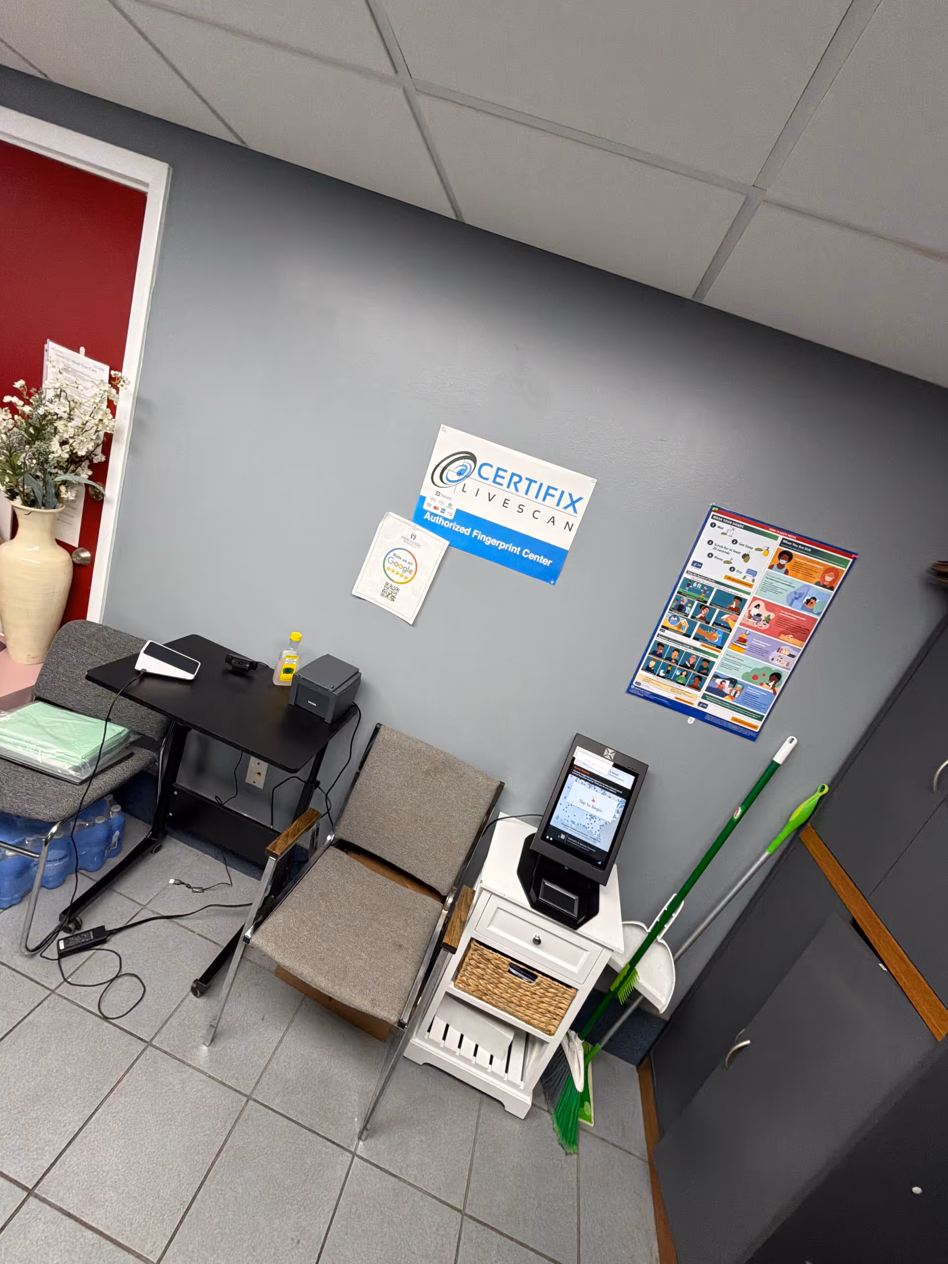 An interior lobby corner with a fingerprint scanner station, chairs, and cleaning supplies.