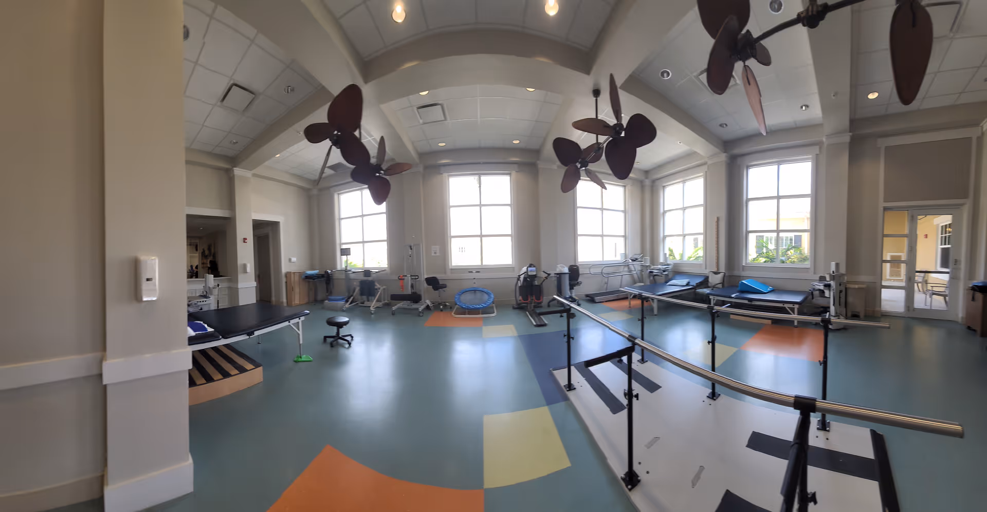 Bright therapy gym with parallel bars, equipment, and large windows in a rehab center.