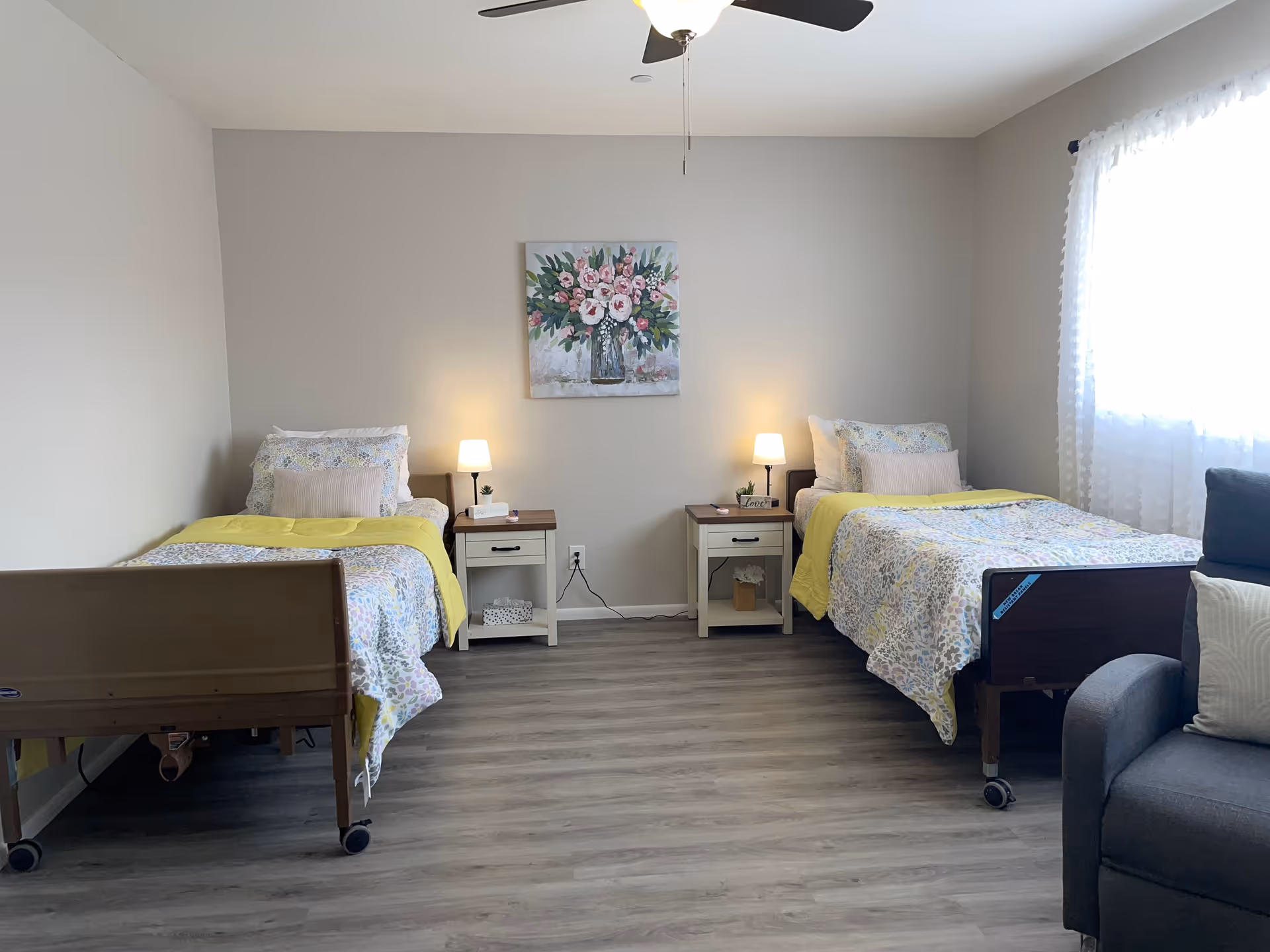 Two single beds with floral bedding, nightstands, lamps, and a painting in a bright bedroom.