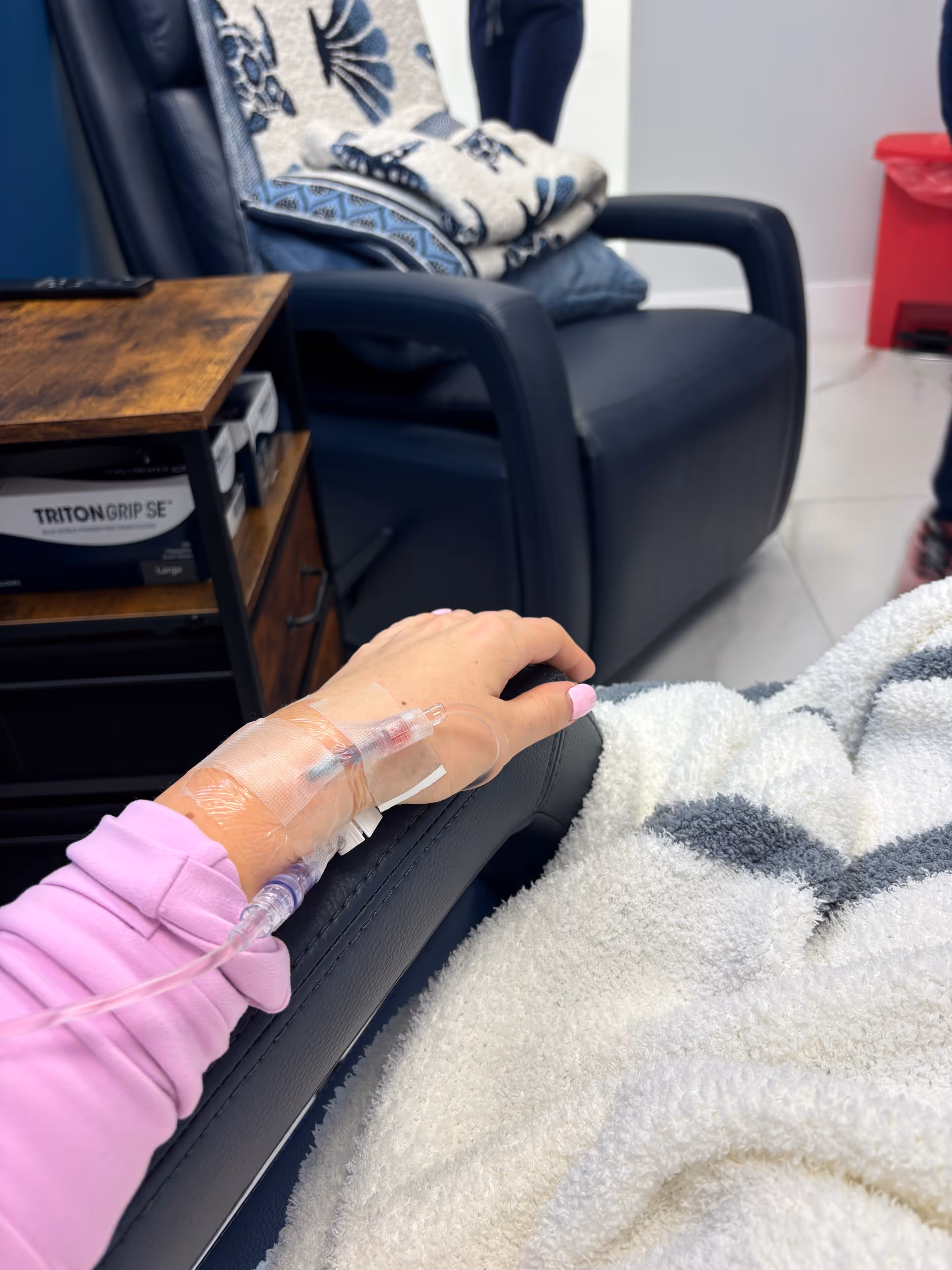 Patient's IV hand rests on a sofa in a bright senior living lounge.