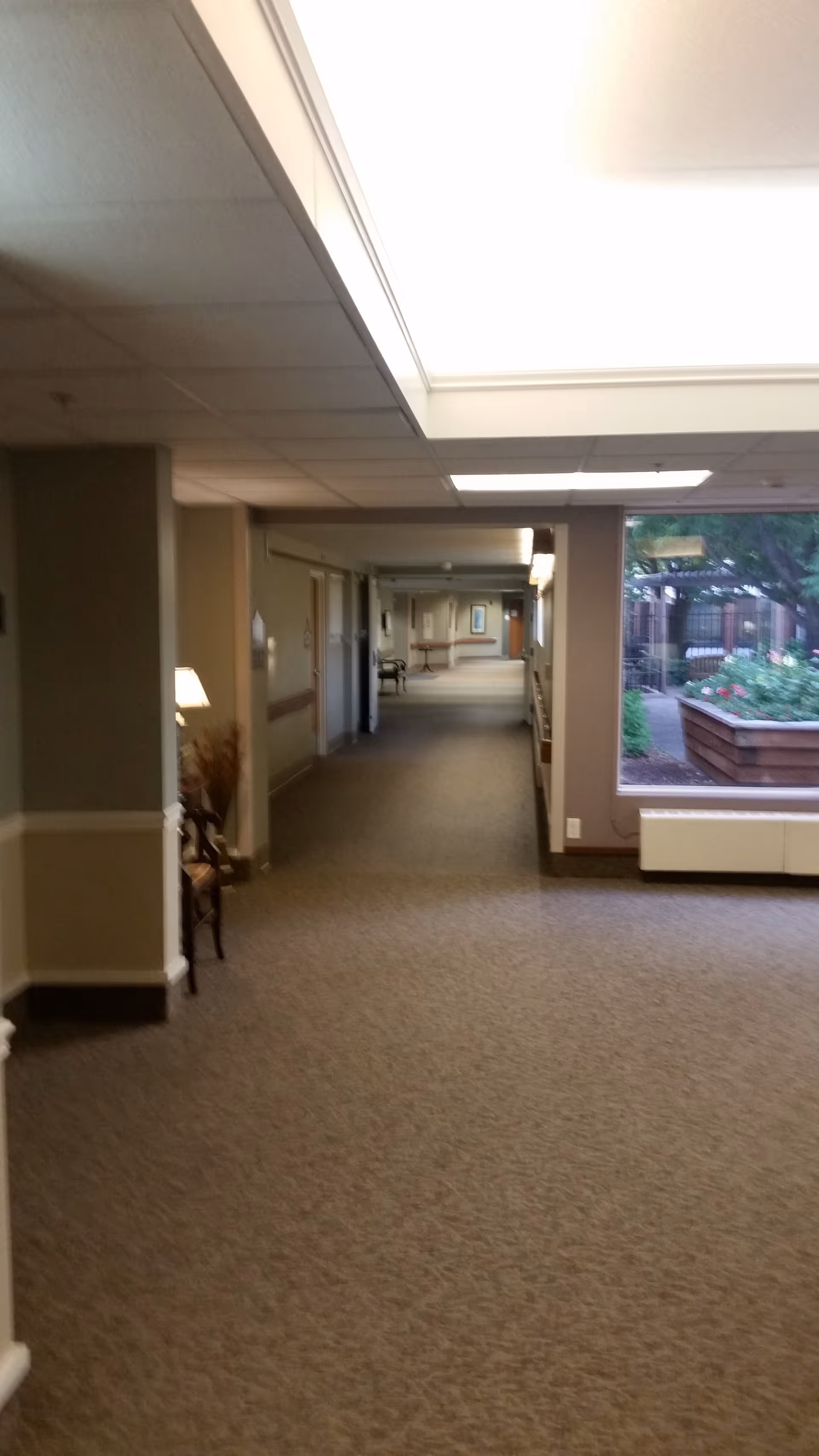 Long interior hallway of Covenant Living facility with beige walls, carpet, and windows.