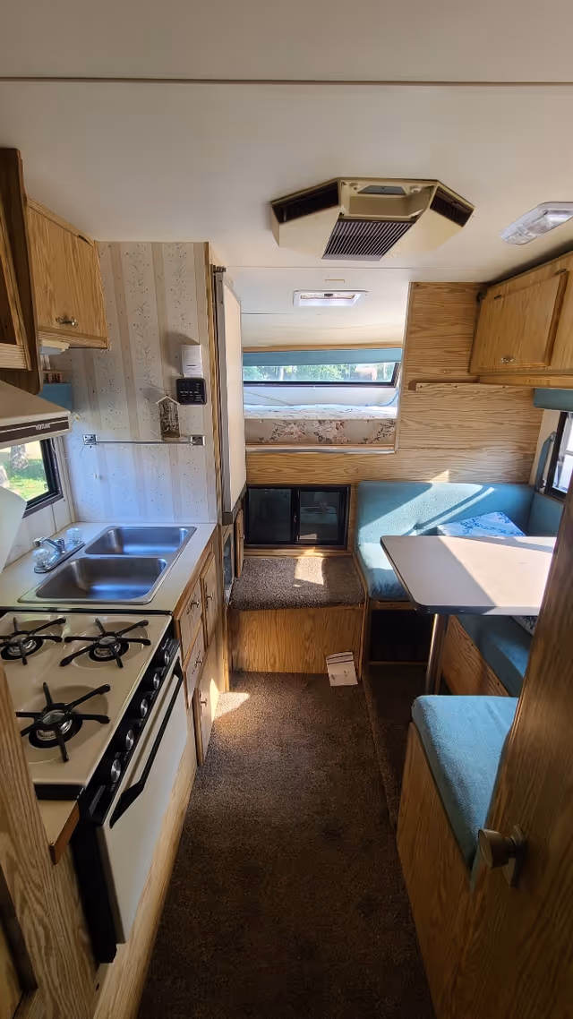 Interior RV-style kitchenette with stove, sink, and dinette seating.