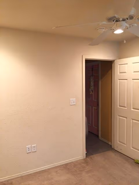Interior of a senior living space with beige walls, ceiling fan, and open doorway.