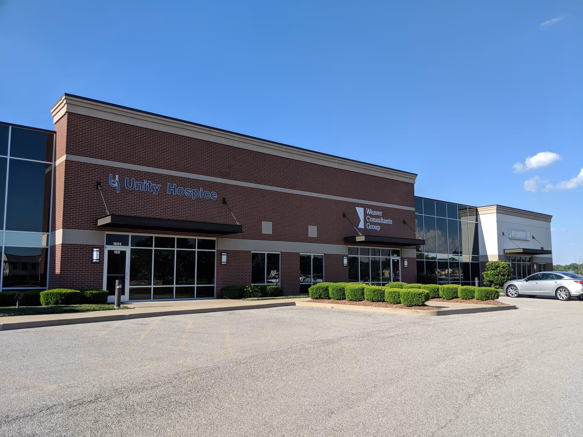Exterior view of a brick Unity Hospice building with glass windows and parking.