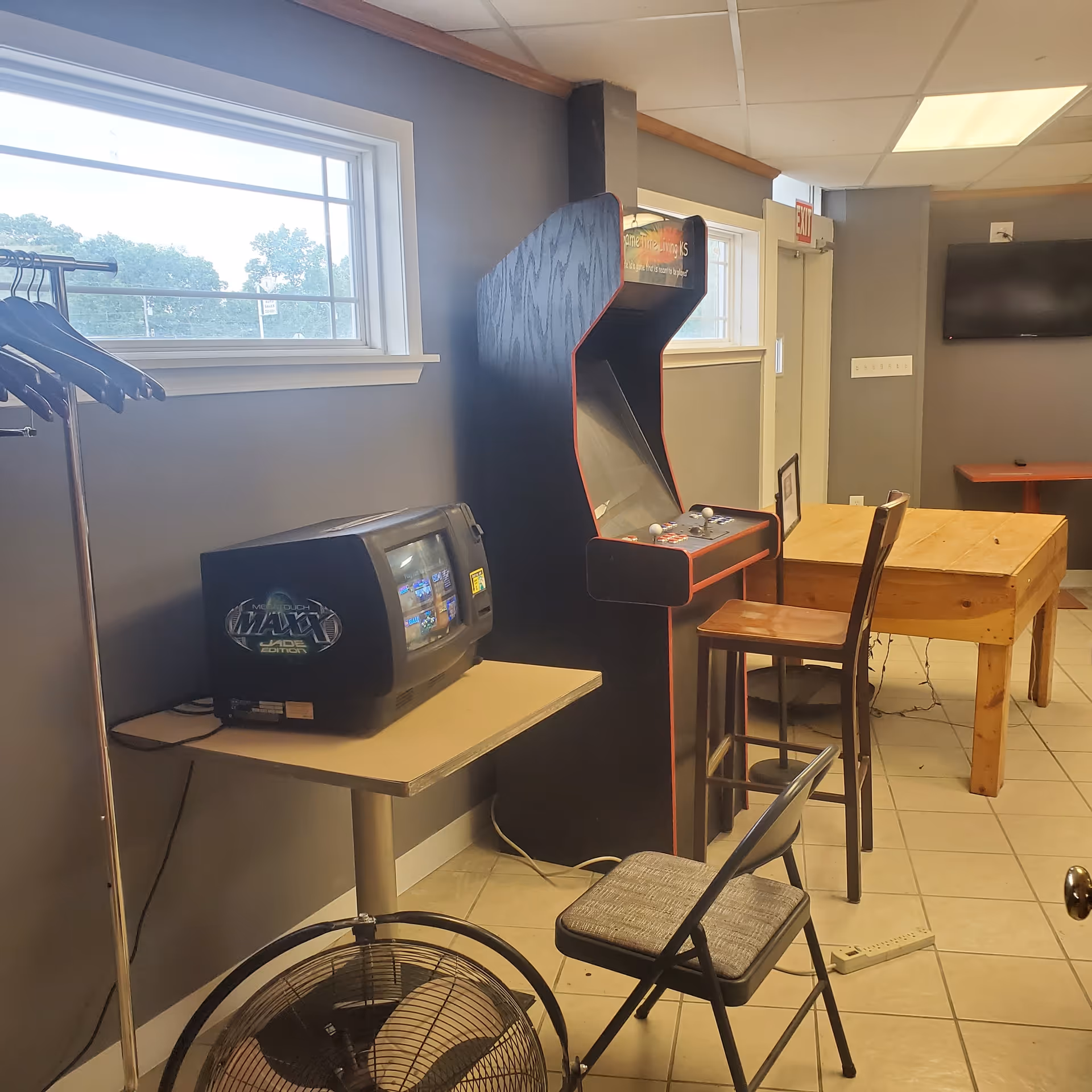 Indoor recreation room with arcade cabinet, small TV, table, chairs, and window.