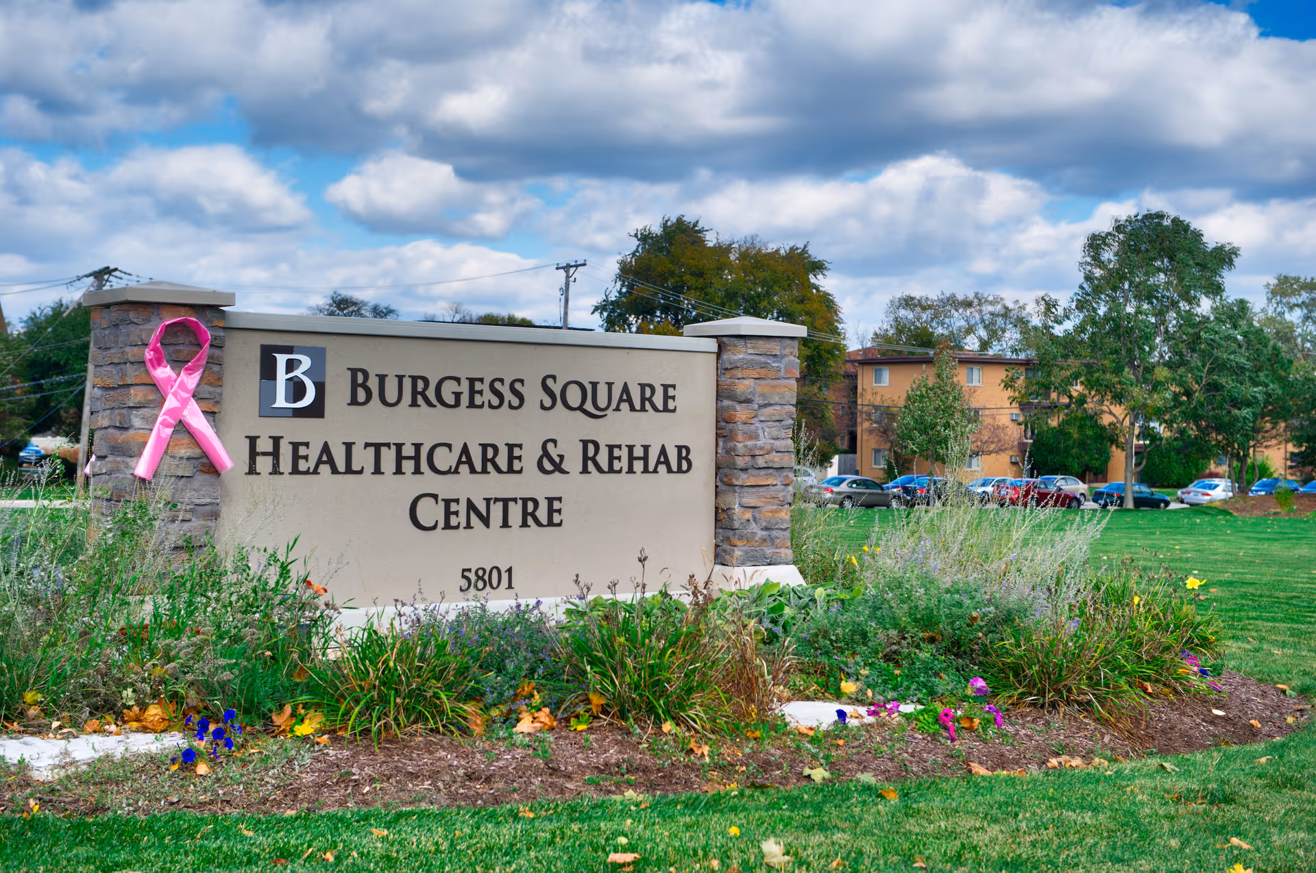 Stone entrance sign reading Burgess Square Healthcare and Rehab Centre with pink ribbon and landscaping