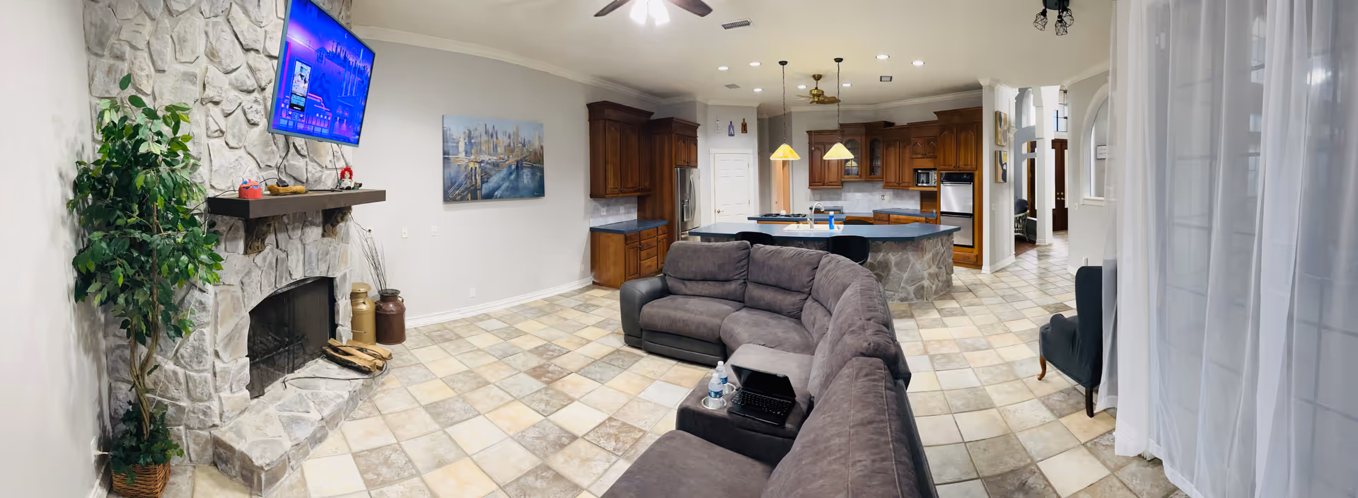 Open-concept living room with stone fireplace, TV, and curved sectional facing the kitchen.