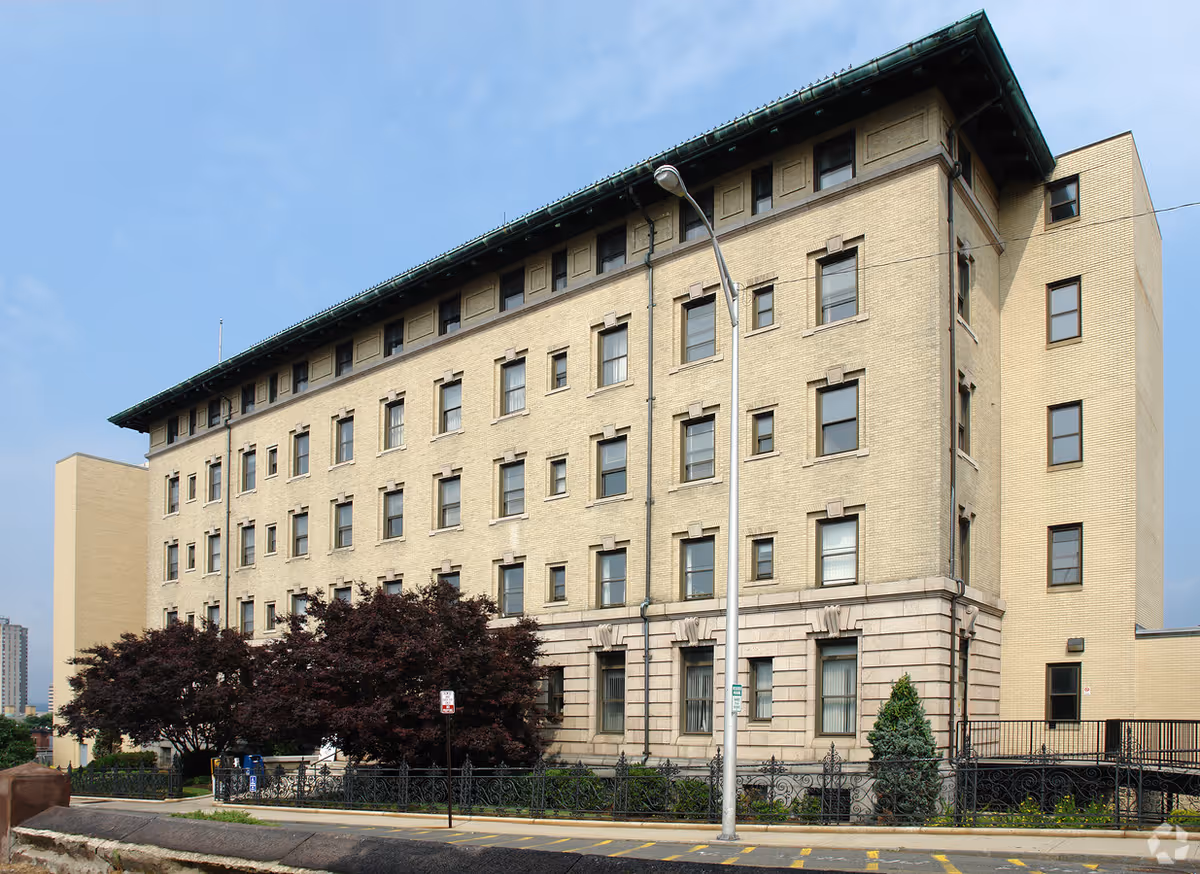 Exterior view of a multi-story beige brick senior care building with trees.