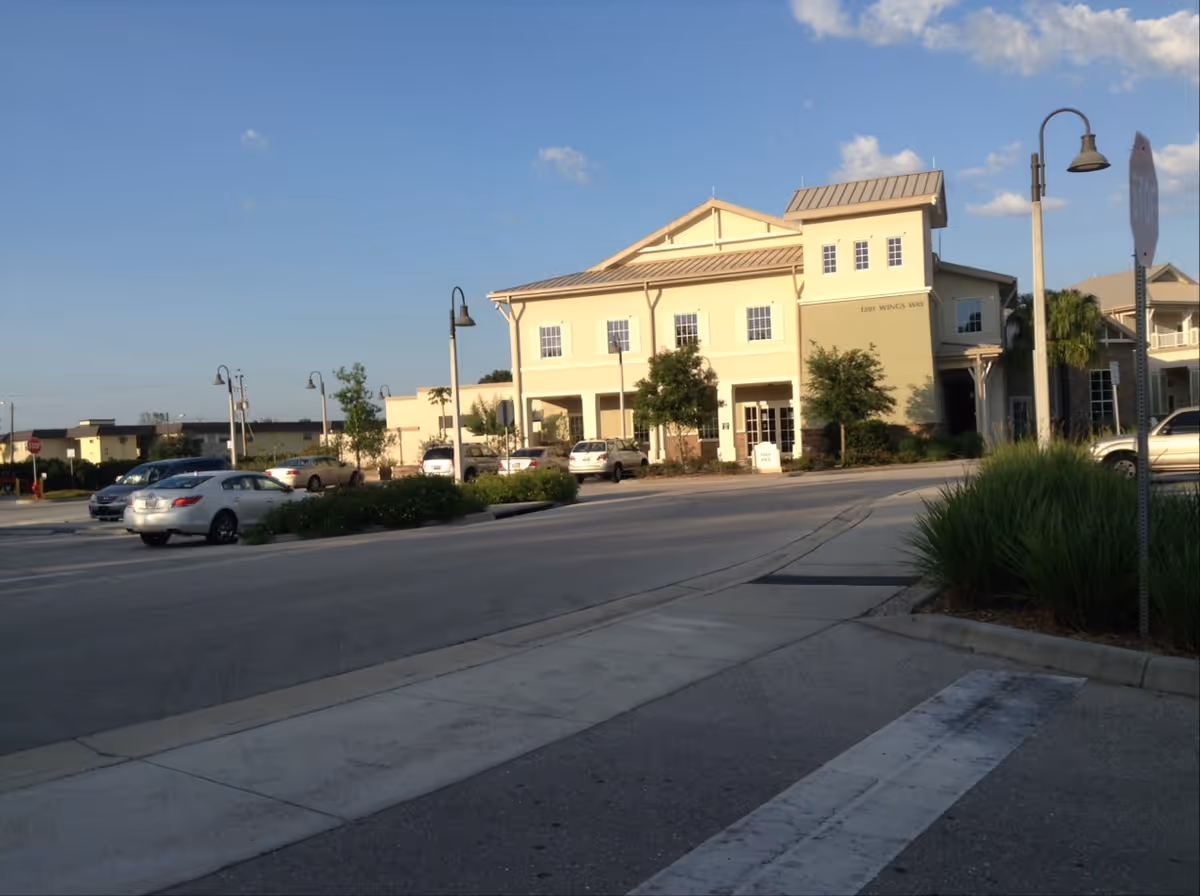 Exterior view of a beige senior living facility with a parking lot and street lamps.