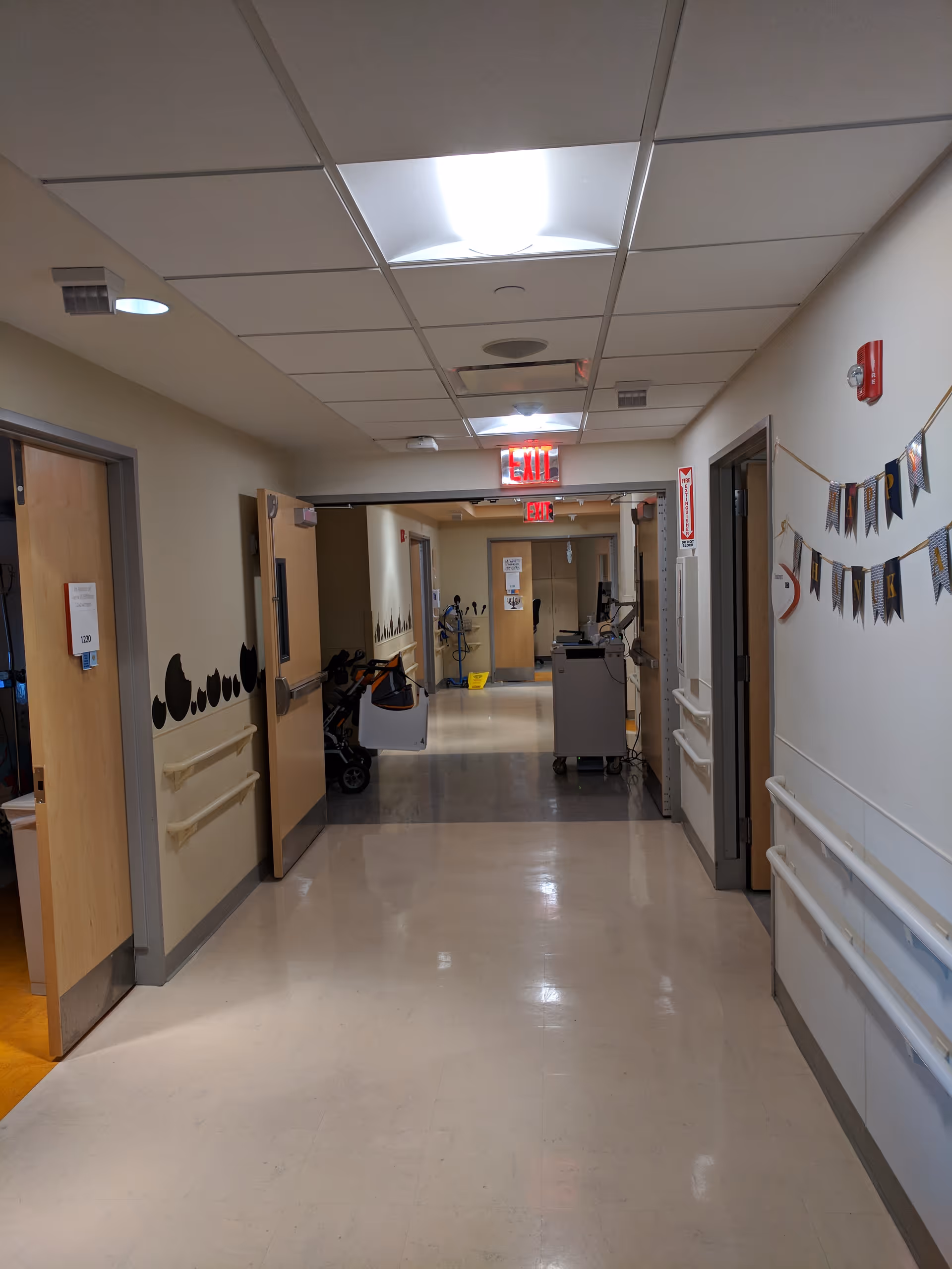 Long hospital hallway with doors, carts, and medical equipment in a clinical facility.