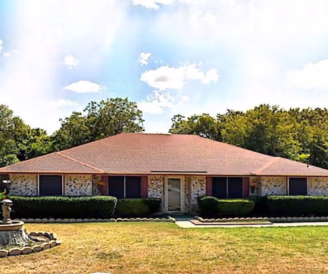 Single-story brick building with stone accents, brown roof, and trimmed hedges in front.