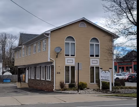Two-story beige building with arched windows and a sign, viewed from the street.