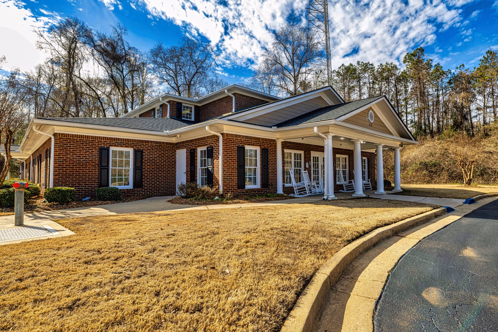 Brick hospice building with white columns and rocking chairs beside a curved driveway.