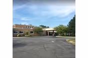 Brick senior living facility front with a covered entrance and surrounding trees.