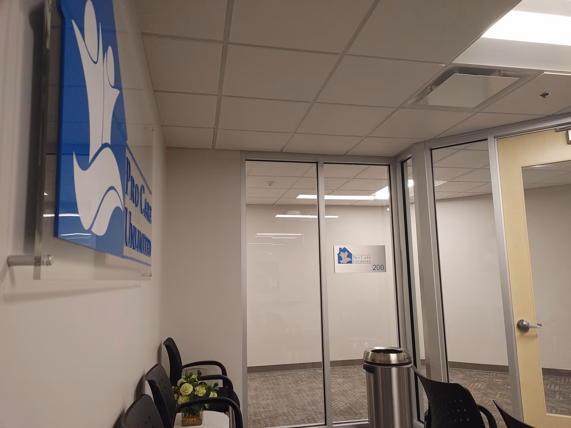 Interior lobby with glass doors, a blue sign, and chairs along the wall.