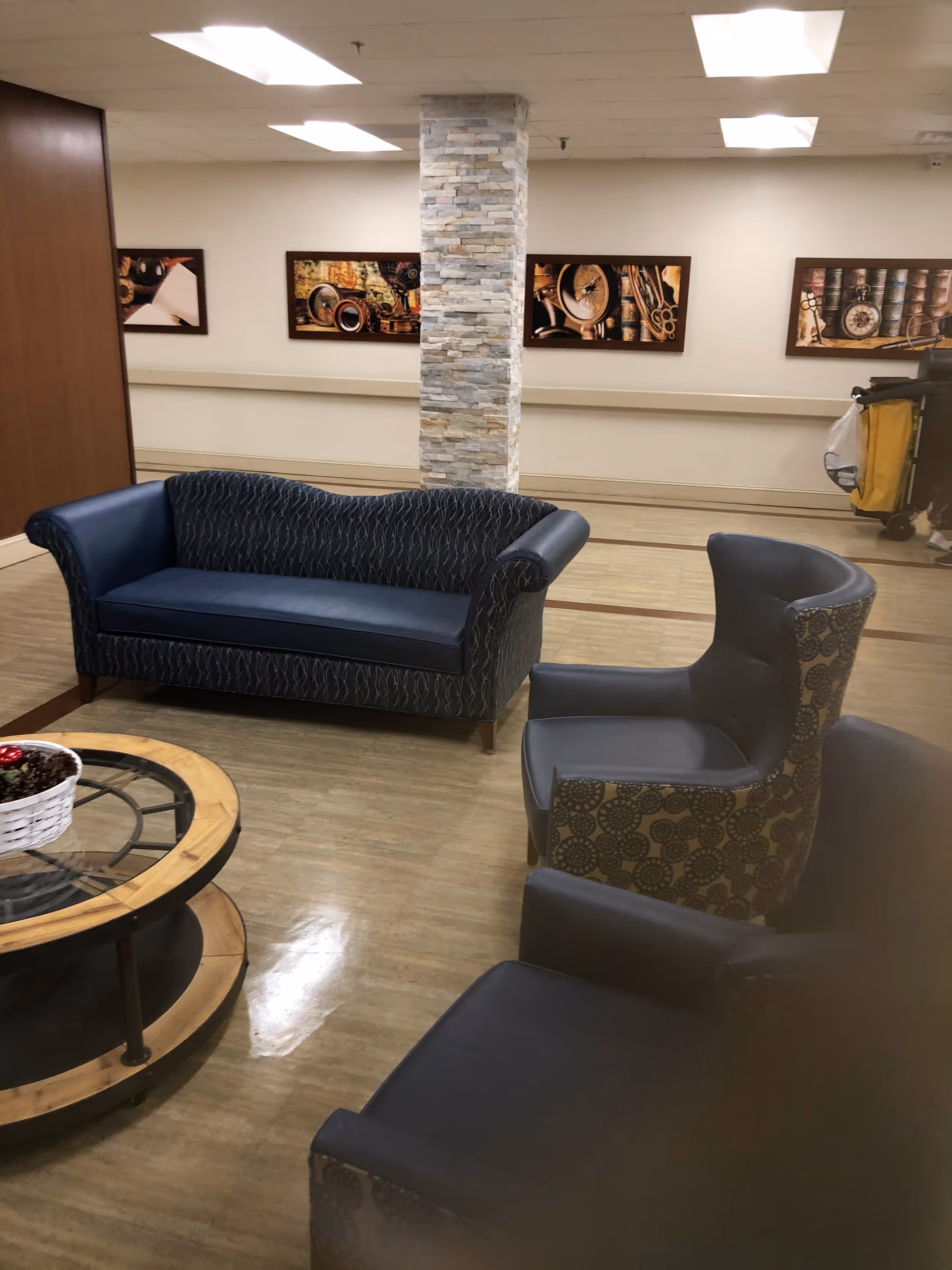 A tiled-floor lounge with blue sofa, patterned chairs, round coffee table, and stone pillar.