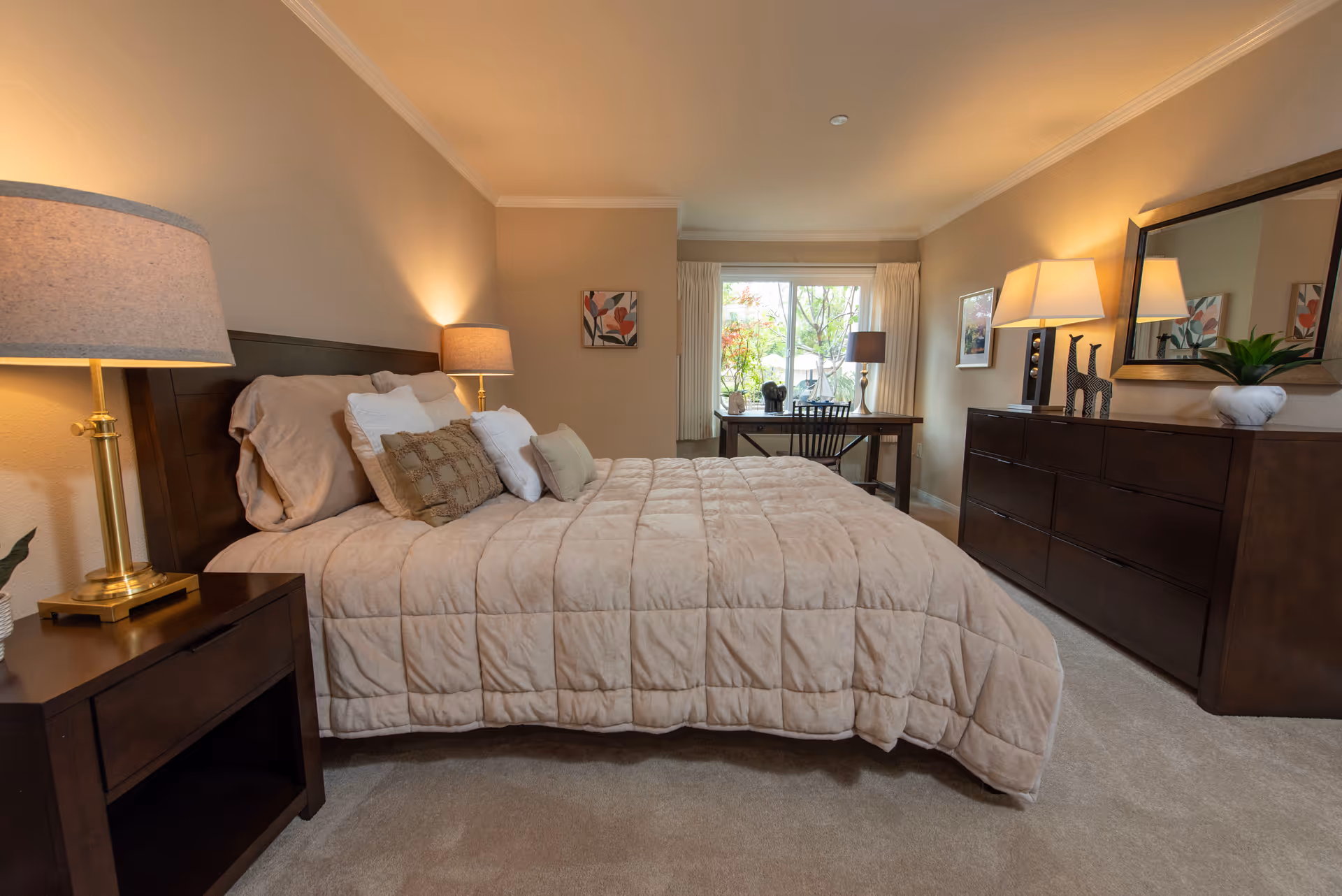 A cozy, well-lit bedroom with a large bed, nightstands, dresser, and a desk by the window.