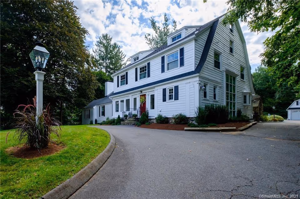White multi-story senior living building with curved driveway and landscaped grounds.