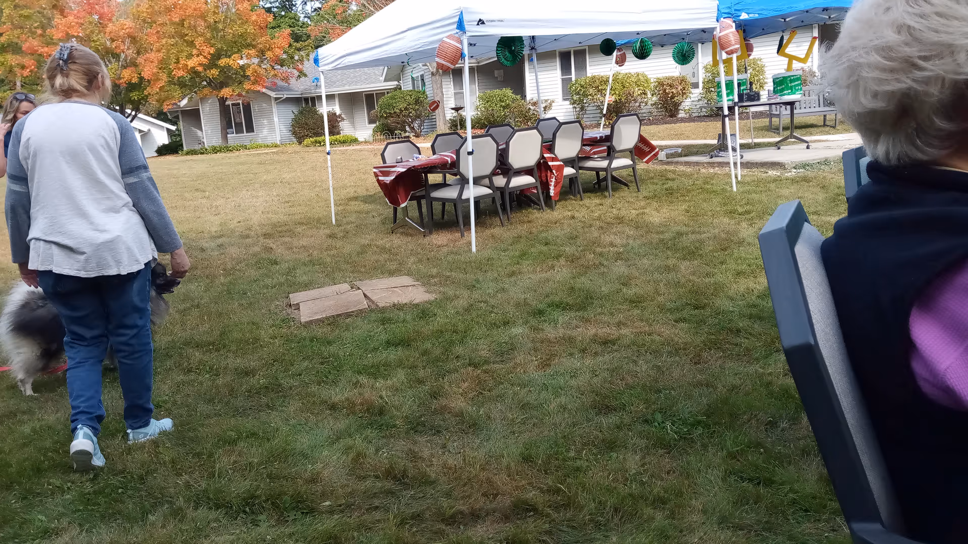 Outdoor event setup at a senior living campus: tent, tables, chairs, and residents.