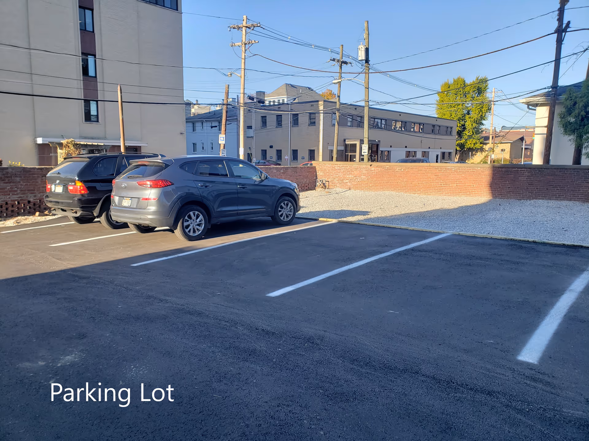 Parking lot with two cars and a brick wall against a cityscape background.