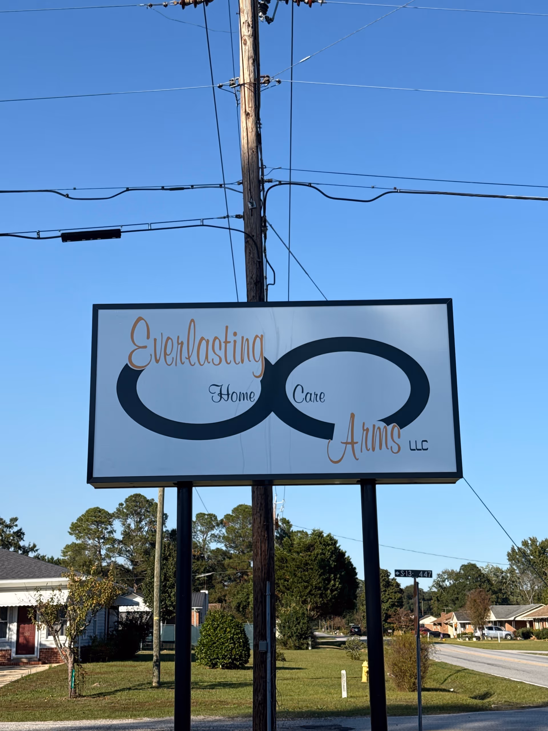 Outdoor sign for Everlasting Arms Home Care LLC along a street with utility lines overhead.