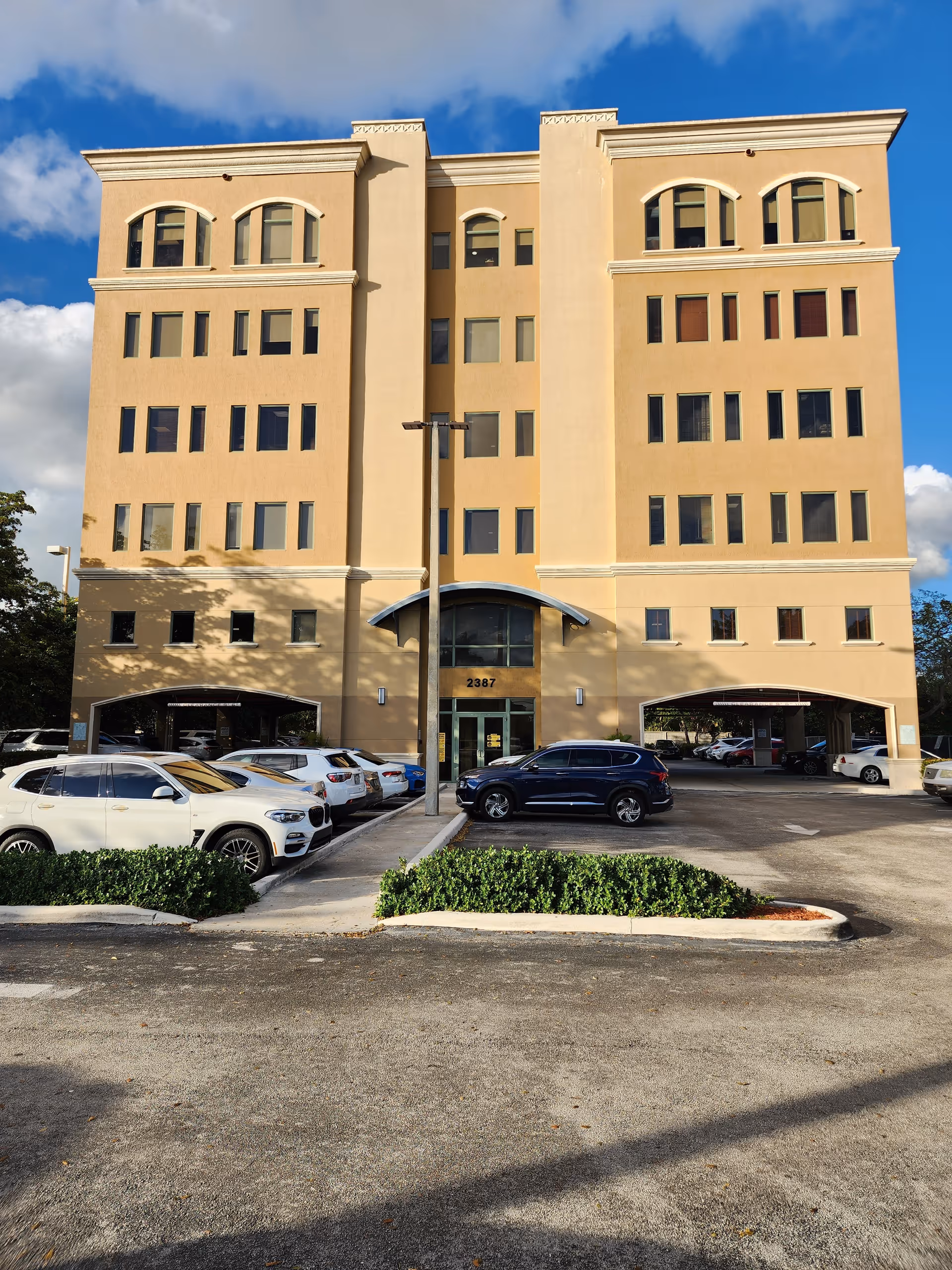 A tall beige building with arched windows and parked cars in front.