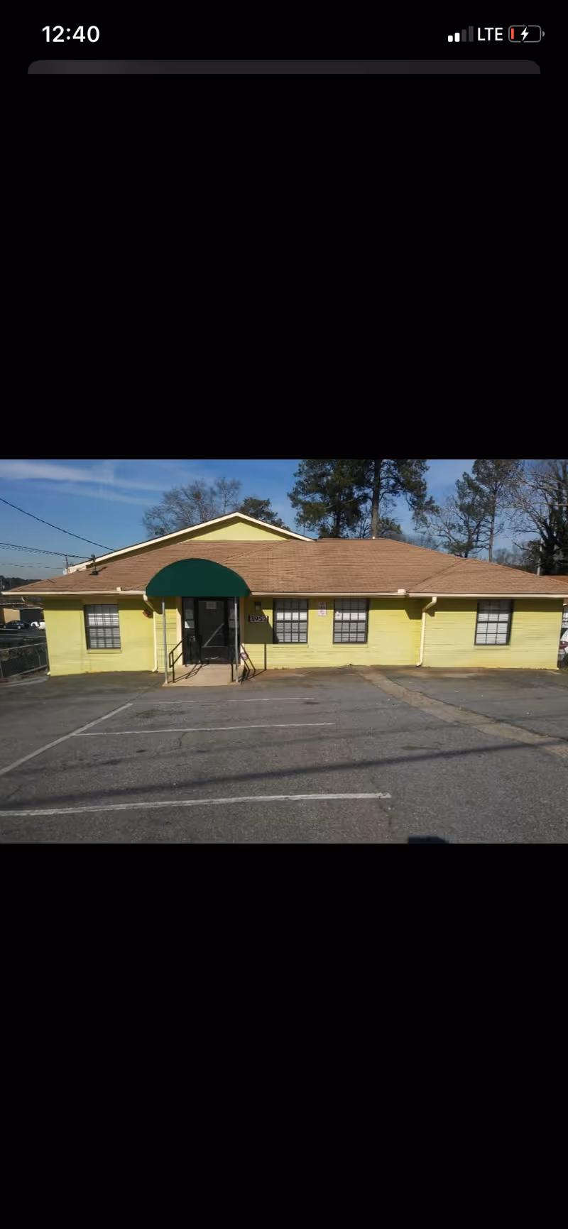 Front of a yellow building with a green awning over the entrance and parking lot.