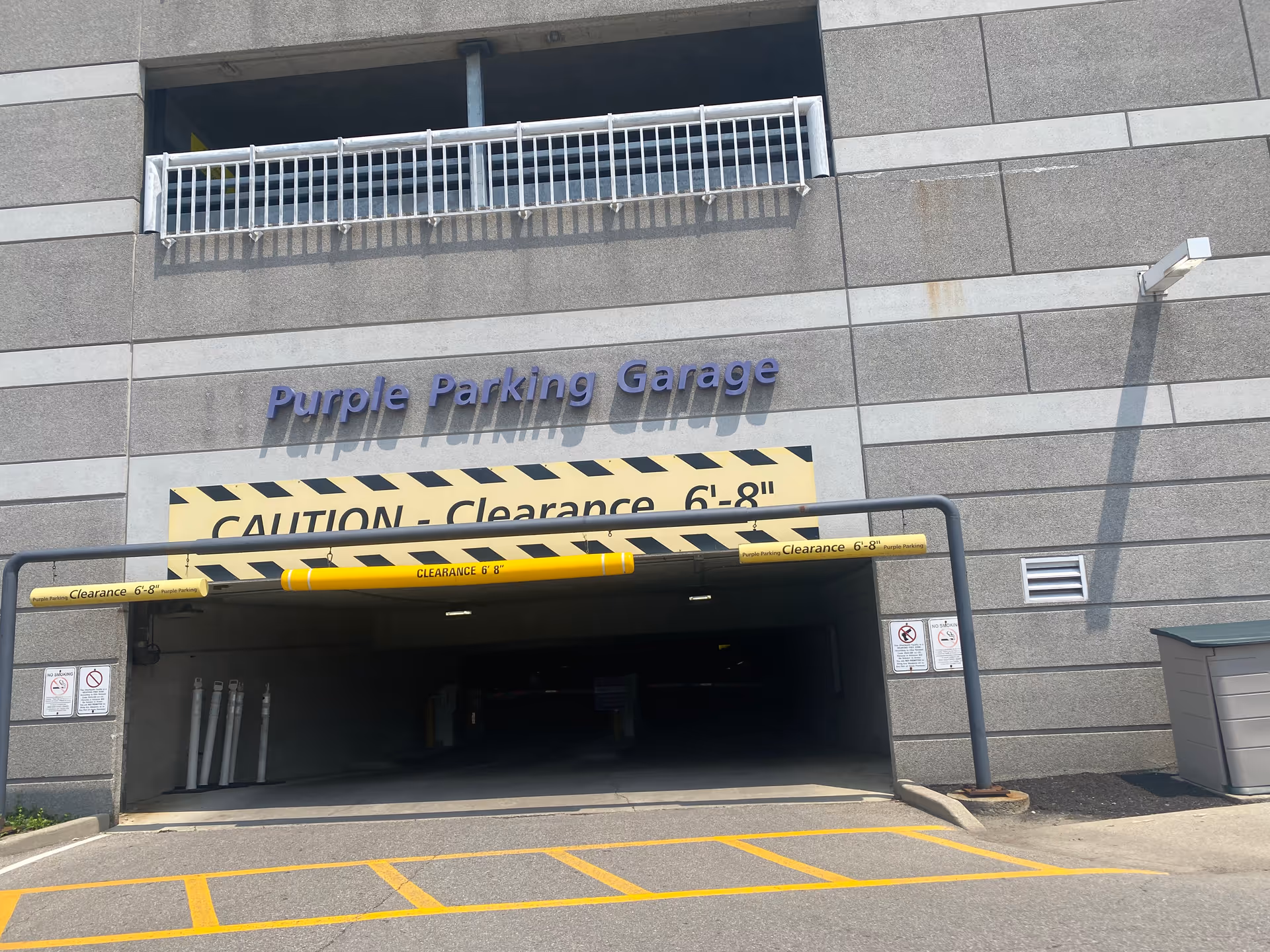 Entrance to a parking garage with yellow clearance bars and Purple Parking Garage sign.