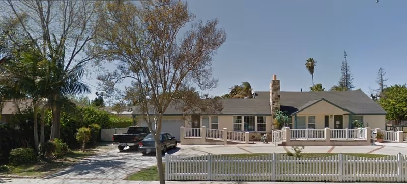 Single-story senior living home with a white railing front porch and fenced yard.