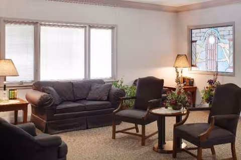 Cozy senior living lounge with sofa, chairs, tables, lamps, and stained-glass art.
