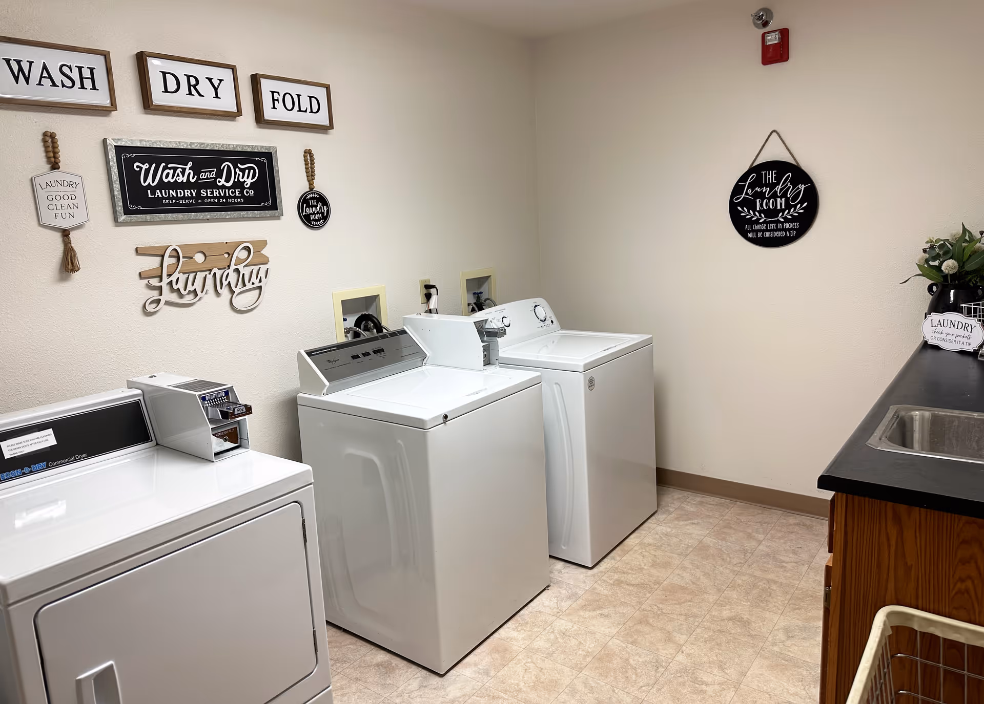 Interior laundry room with three washing machines, a sink, and decorative wall signs.