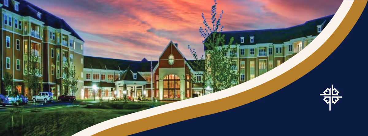 Exterior view of a large senior living facility building at sunset with a colorful sky, well-lit entrance, and landscaped grounds.