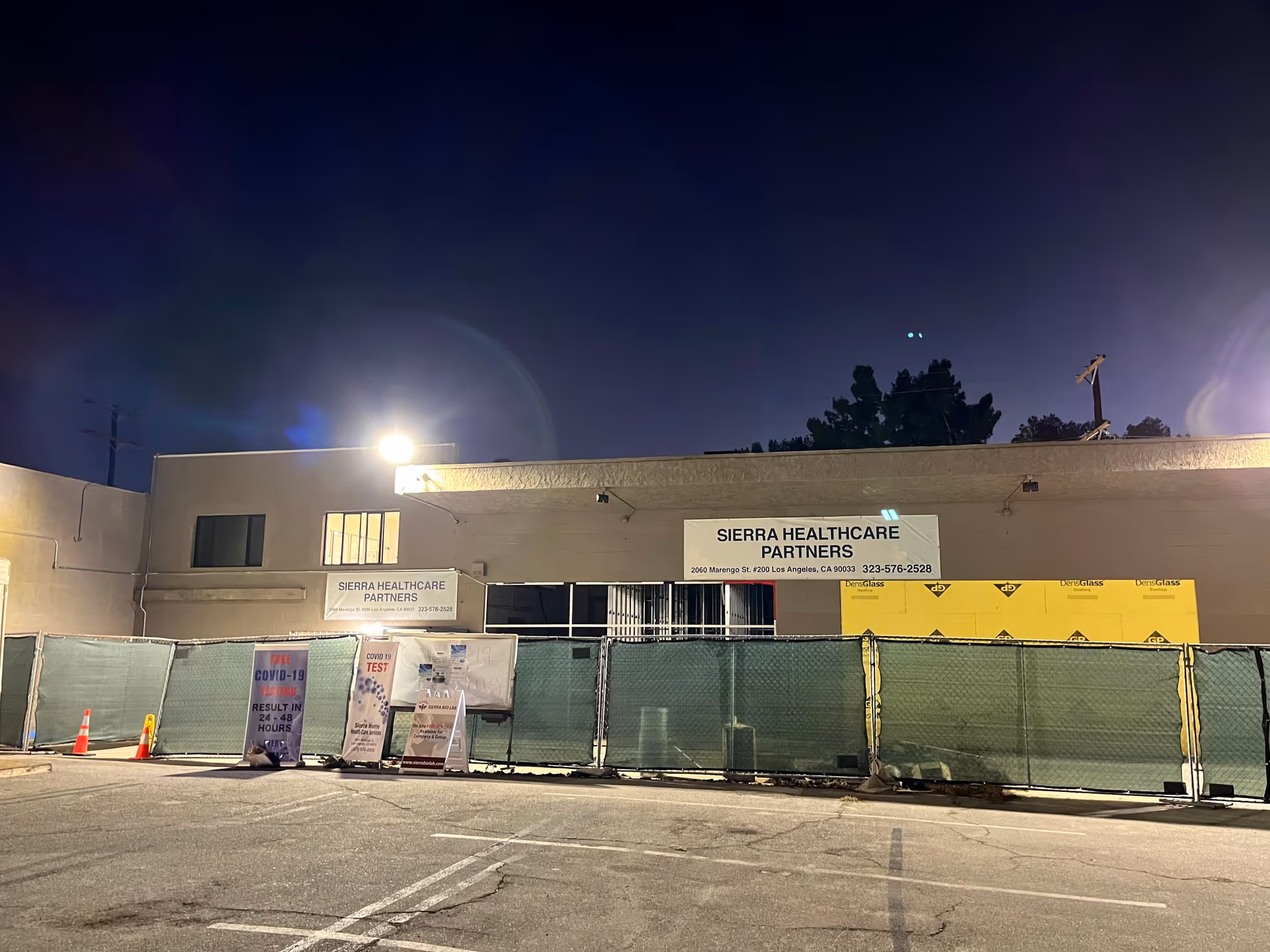 Nighttime exterior of Sierra Healthcare Partners building behind a green construction fence.