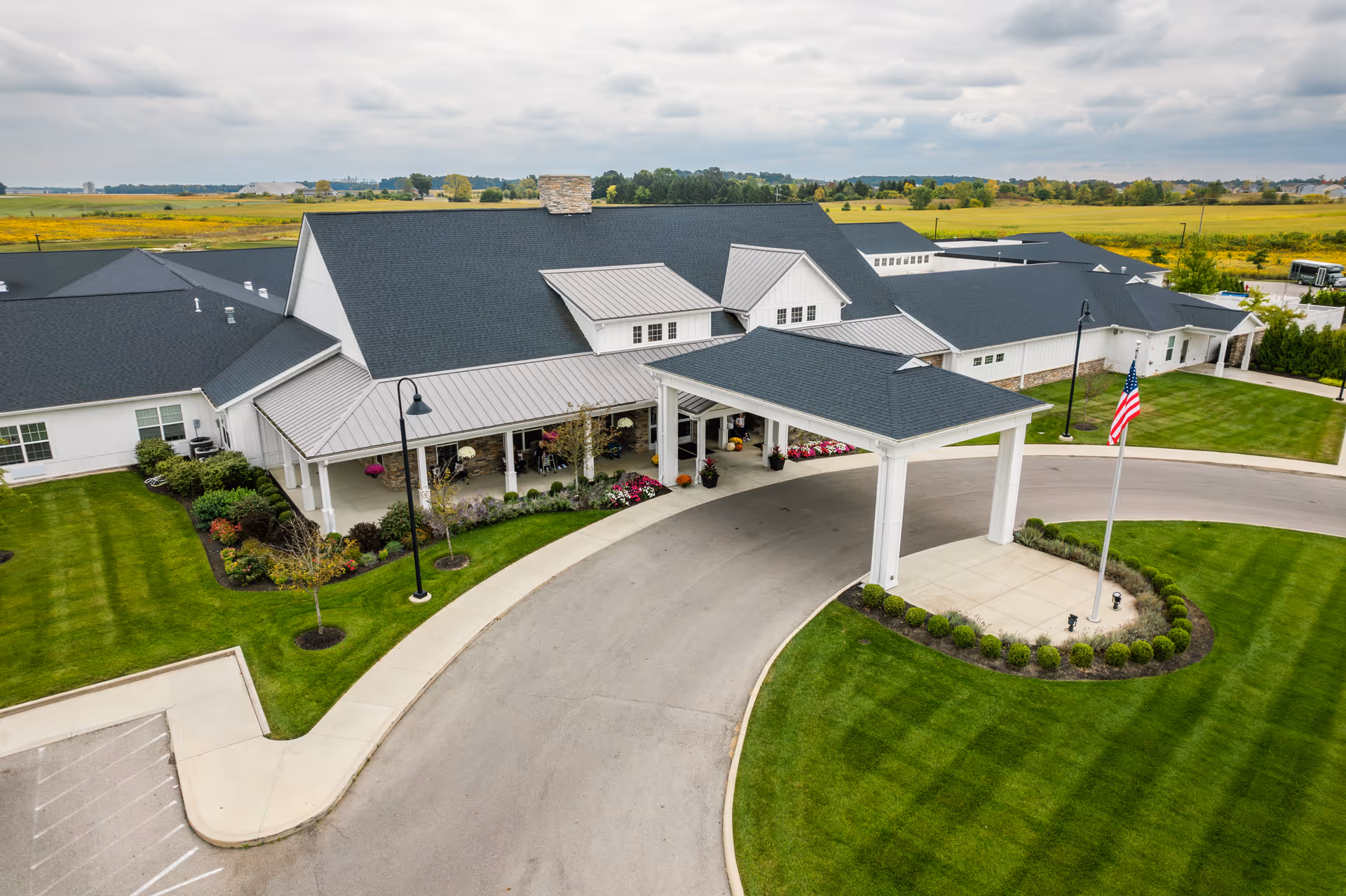 Aerial view of Walnut Crossing showing the facility's covered porte-cochere entrance, manicured lawns, and an American flag.