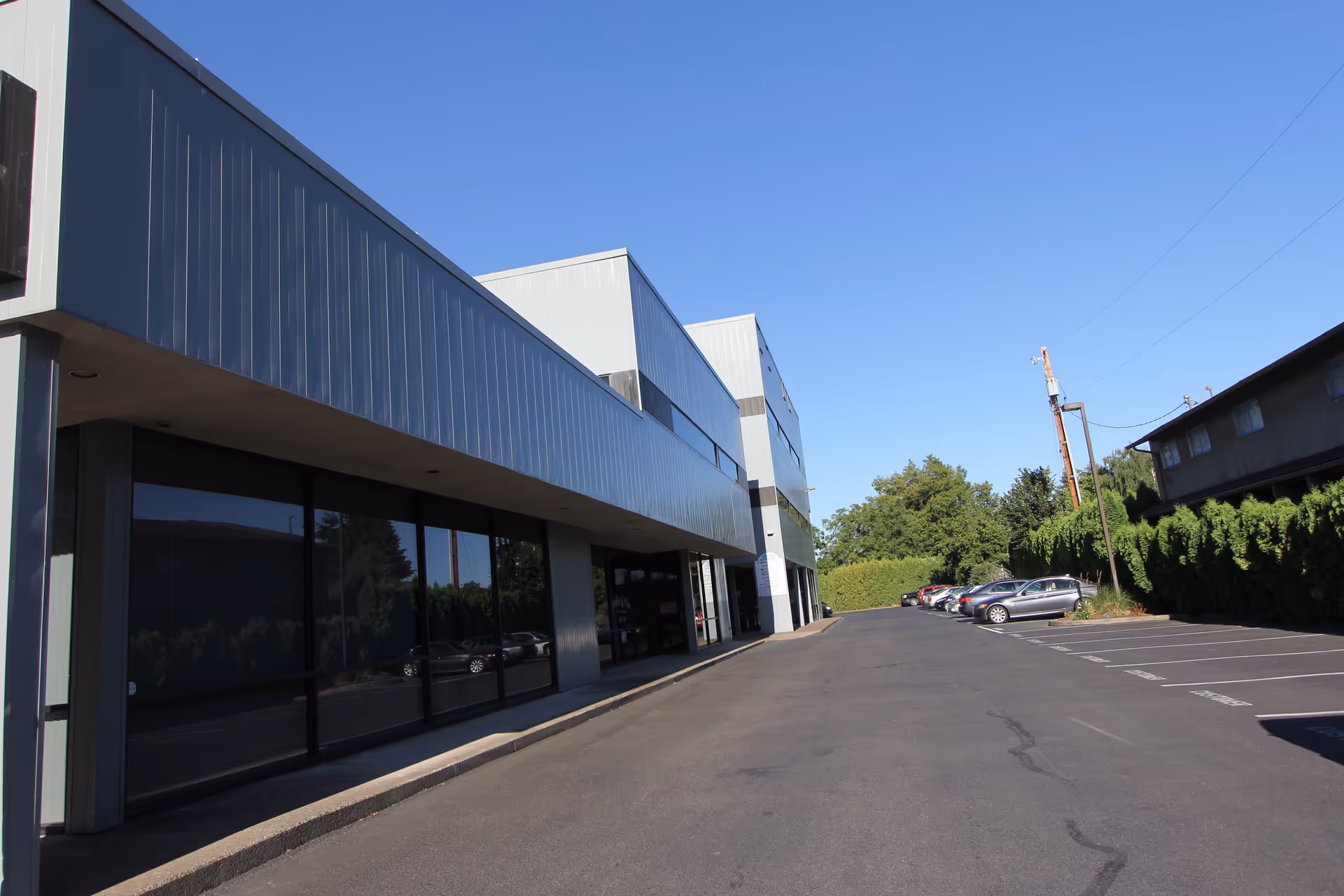 Exterior view of a modern gray building with storefront windows and a parking lot.