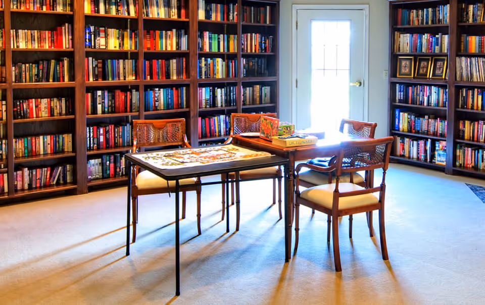 Cozy library room with tall bookshelves, a central table, and four chairs.