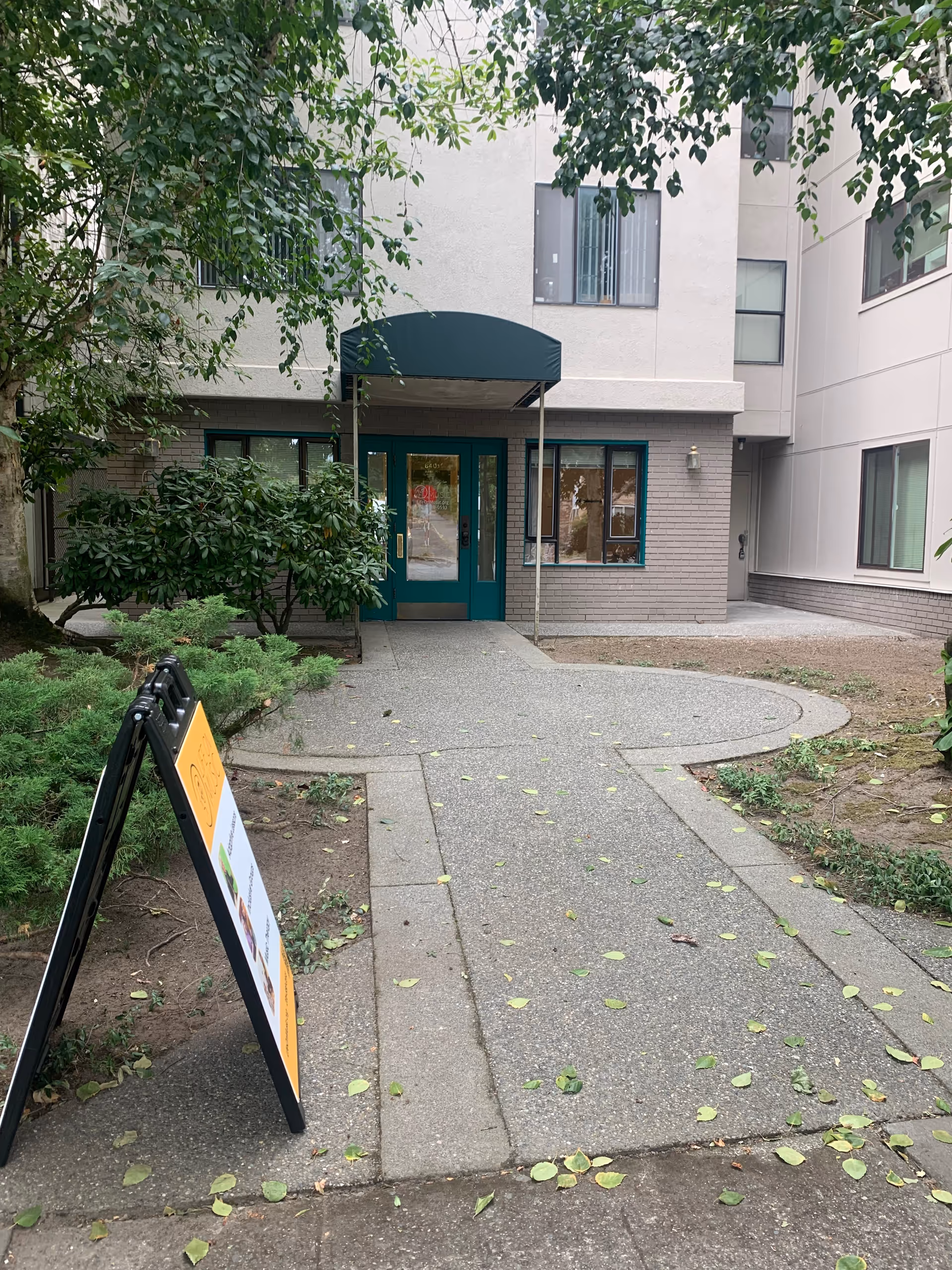 Exterior entrance to a senior living facility with teal doors and a curved walkway.