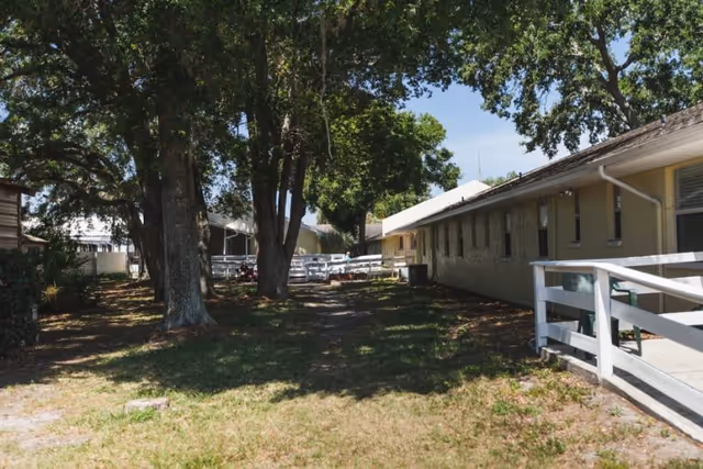 Outdoor view of Angels Senior Living at North Tampa, with trees, walkway, and single-story buildings.