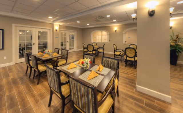 Well-lit dining area with multiple set tables, upholstered chairs, and folded yellow napkins.