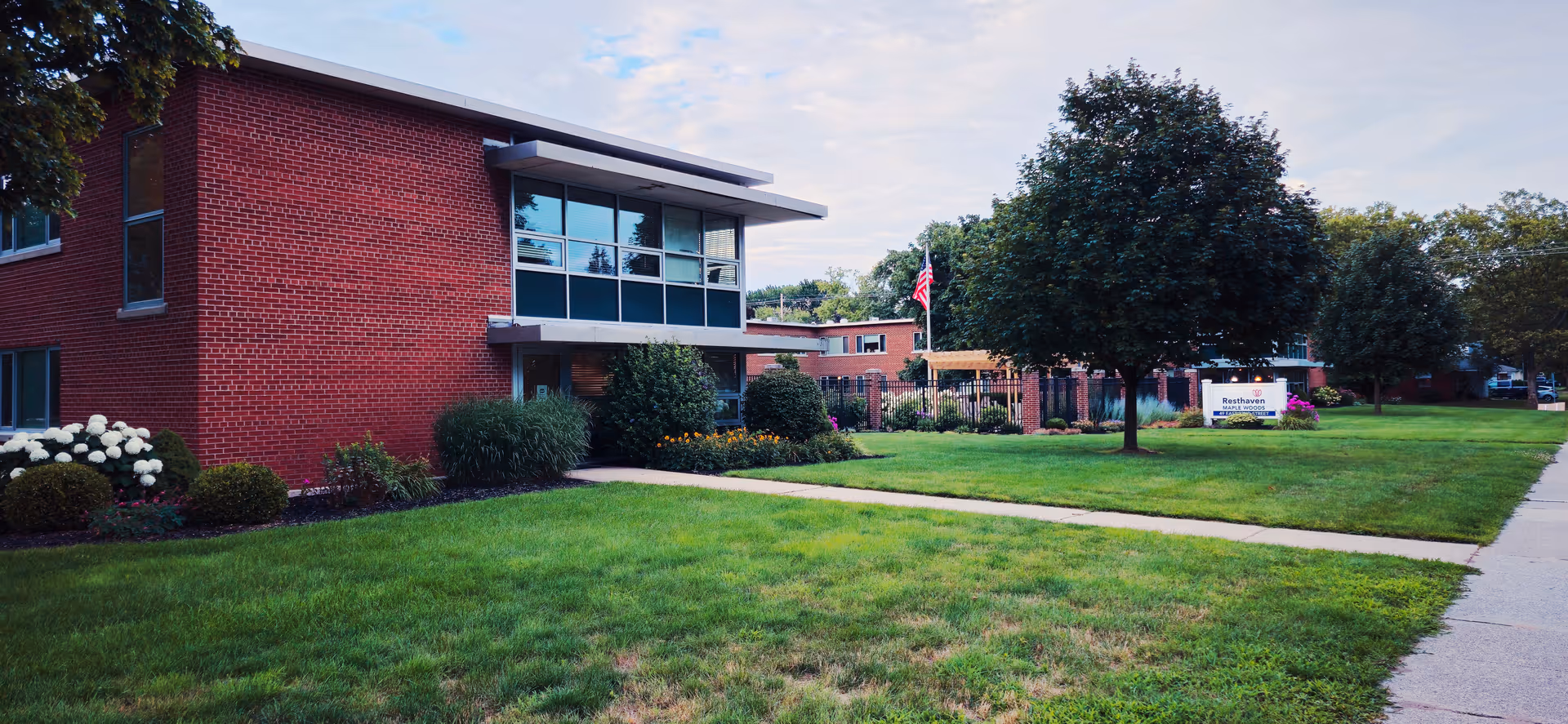 Red brick senior living building with manicured lawn and trees.
