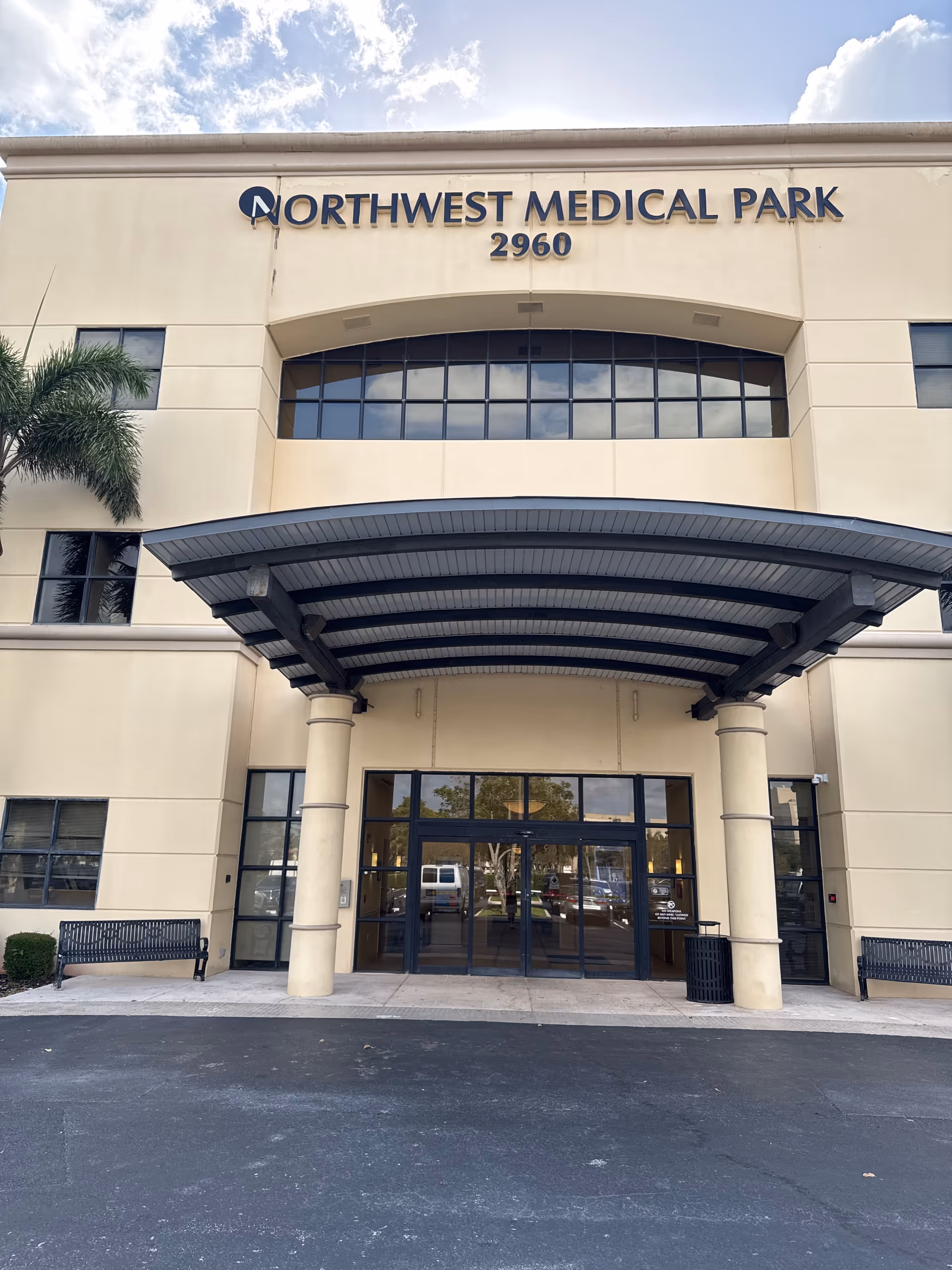 Front view of a beige medical facility with curved canopy and glass entrance doors.