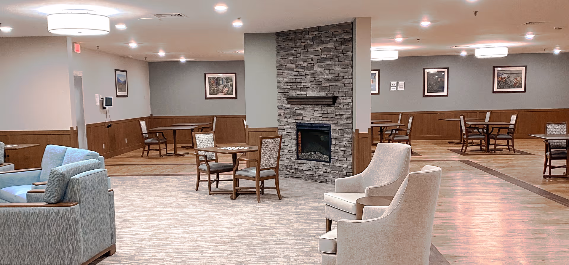Spacious indoor lounge with sofas, armchairs, and tables surrounding a stone fireplace.