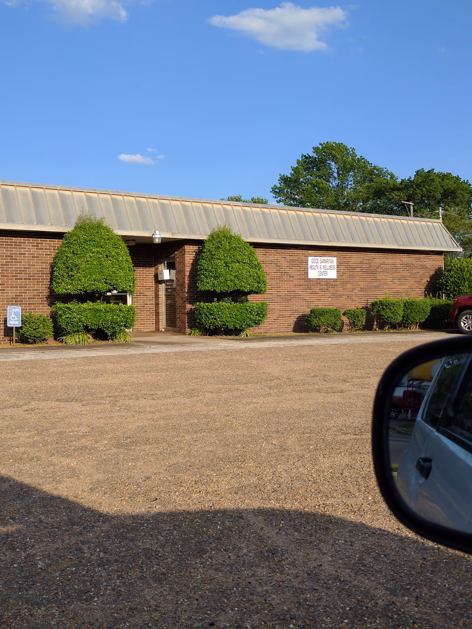 Exterior brick administrative office with trimmed shrubs and car mirror in foreground.