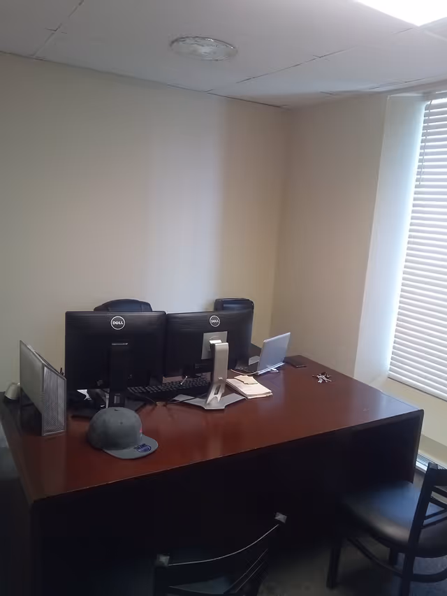 Office desk with two Dell monitors, a laptop, papers, and a cap.