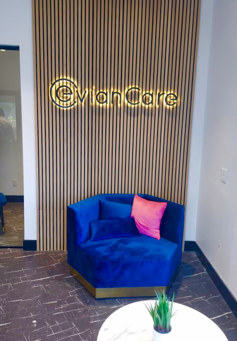 Lobby area with backlit EvianCare sign on striped wooden wall and blue chair.