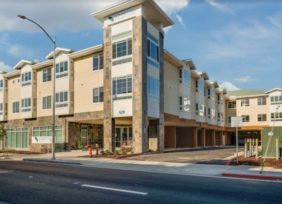 Front exterior of Sonnet Hill Senior Living, a three-story building with stone accents, covered parking bays, and street frontage.
