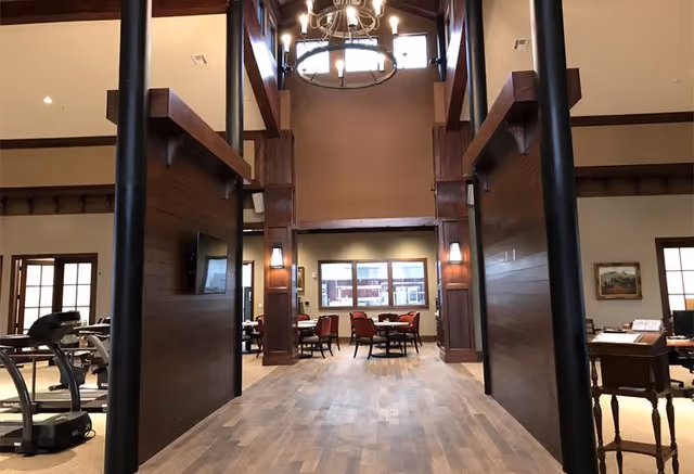 High-ceilinged common area with wooden beams, a chandelier, seating tables and an exercise machine.