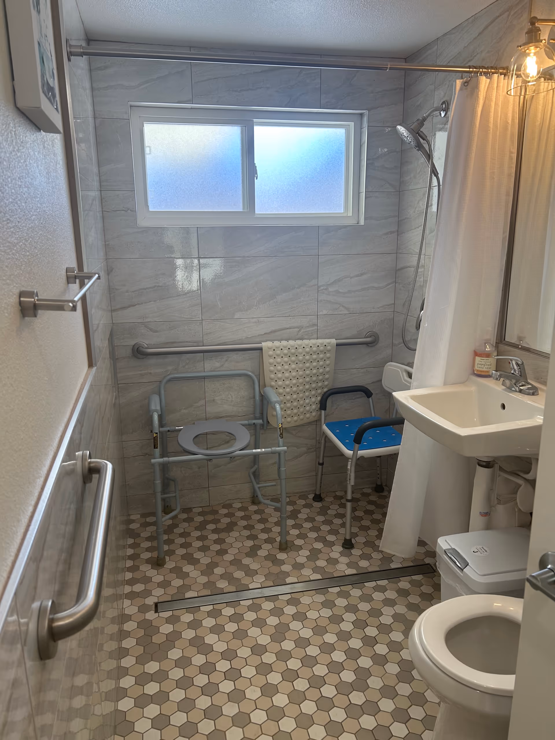 Accessible bathroom with grab bars, shower chair, sink, and toilet.