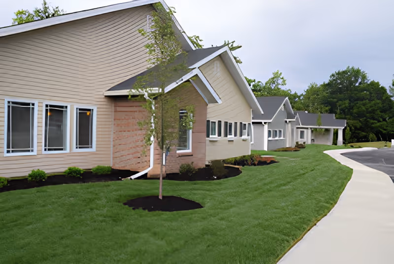 Exterior view of a single-story senior living building with connected units, a manicured lawn, and a sidewalk leading past the entrance.