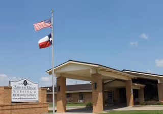 Front entrance of a senior living facility with flags and brick columns.